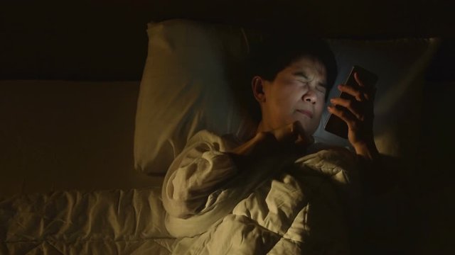 Middle age woman using a smartphone in her bed at night .