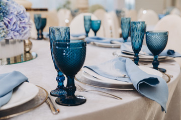 festive tables in the banquet room are decorated with compositions of white and blue flowers, on the tables are plates with napkins, glasses, candles, a wedding dinner