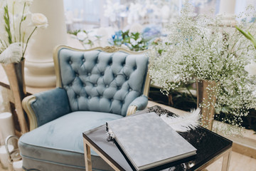 in the white room is a vintage armchair, on a black coffee table is a book and a vase of flowers