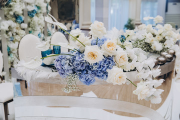 festive tables in the banquet room are decorated with compositions of white and blue flowers, on the tables are plates with napkins, glasses, candles, a wedding dinner