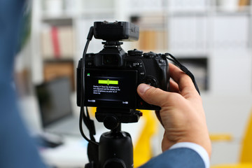 Male arms in suit mount camcorder to tripod making promo videoblog or photo session in office...