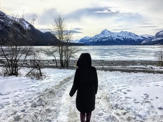A woman walking along an unknown path towards a frozen lake in a beautiful winter landscape on Abraham Lake, Alberta, Canada.  The Rocky Mountains are in the background.