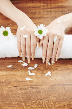 Hands of woman with creative manicure on fresh towel and daisy flowers and petals