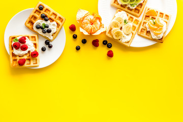 Beautiful yummy snacks. Waffles with cream and friuits on yellow background top-down frame copy space