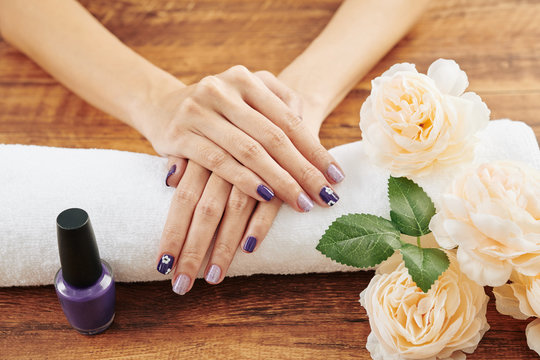 Hands of woman with fresh purple manicure with simple design on soft white towel