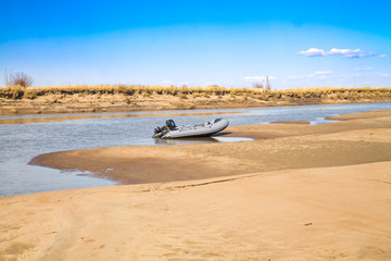 Fototapeta premium River motor boat near sandy river bank with golden dunes and blue water