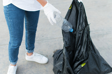 Woman in white globes puting plastic bottle in trash bag