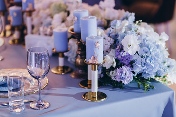 the festive table at the wedding party is decorated with flower arrangements, on the table are plates with napkins, glasses, candles, cutlery