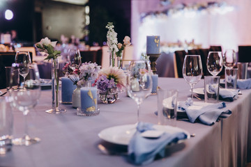 the festive table at the wedding party is decorated with flower arrangements, on the table are plates with napkins, glasses, candles, cutlery