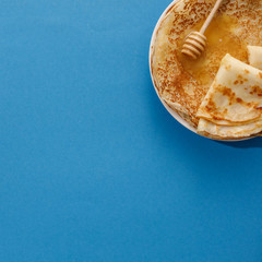 Tasty homemade pancakes with honey on a blue background. Top view, close-up. Traditional holiday celebration concept. Russian translation wide and happy Shrovetide Maslenitsa.