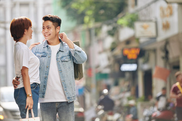 Beautiful happy young Vietnamese couple hugging in the street after shopping together