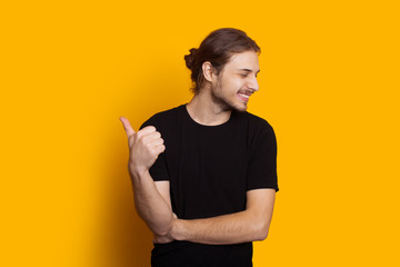 Dressed in black caucasian man with long hair and beard is pointing up while smiling and posing on...