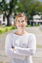 Confident pretty young woman folding hands and looking at camera when spending time outdoors on summer day