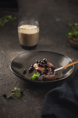 Chocolate muffin with blueberries in black plate on dark background with coffee