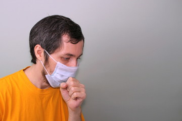 Middle-aged adult man in a yellow T-shirt on a gray background in a medical mask sneezes covering his face with his hand. Cough, fever. Disease protection coronavirus epidemic problem from China