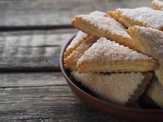 Homemade shortbread puff pastry Triangle in a brown plate on a wooden ancient background. Side view. Place for text.