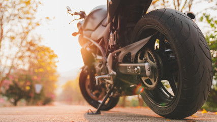 The part of the motorcycle parked on the road is warm ligth. . - obrazy, fototapety, plakaty