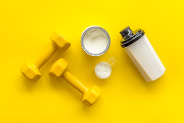 Sport nutrition. Whey protein, shaker, dumbbells on yellow background top-down flay lay