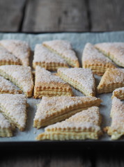 Homemade sandwich puff pastry chocolate cookies on a black baking sheet from the oven. Wooden ancient rustic table. View from above.