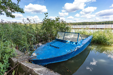 old wooden blue boat on the bank of a wide river in sunny day