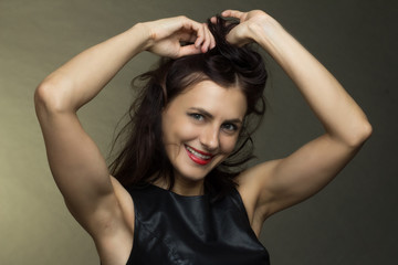 a brunette in a black leather sleeveless blouse poses on a gray background