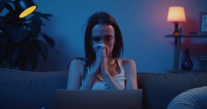 Front view of young girl crying hardly while watching bad news on her laptop. Upset young woman with tears on her face using paper hanierchief. Concept of tragedy, drama and emotions.