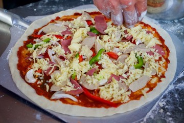 The making process of supreme pizza, arranging raw ingredients on the dough before baking.