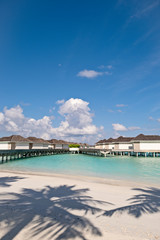 Fototapeta na wymiar Ocean water villas and wooden jetty with the bright blue sky and the crystal clear sea water of Maldives, vertical composition