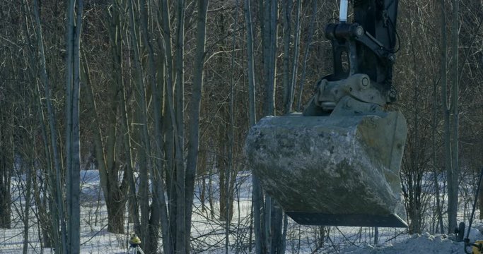 Excavtor bucket turning on winter construction site - close up - slow motion