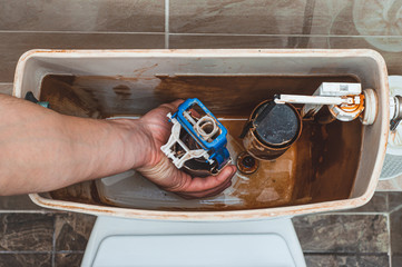 Unscrewing the fittings for draining the water in the toilet flush tank by hand yourself.