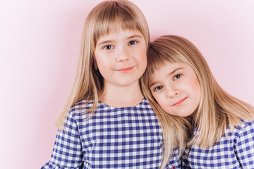 Happy adorable twin blodnie caucasian girls together having fun, hugging and playing. Smilling happy kids. Childhood, twins, friendship concept 