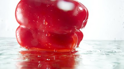 Closeup slow motion video of fresh raw red bell pepper falling in water and splashing droplets - Powered by Adobe