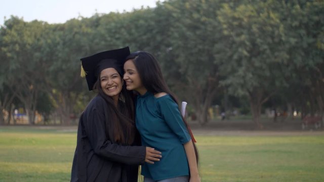 Beautiful Indian girl coming to congratulate her best friend on university graduation. Pretty young female friend hugging her childhood friend on completing her degree on the graduation day - educa...