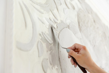 female worker puts putty mortar on a wall with a bas-relief