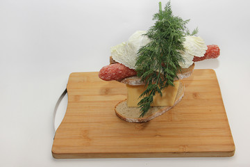 cheeseburger made of bread cheese sausage and dill sprigs on a cutting board