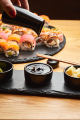 Hand  pouring soy sauce (Shoyu) from little jug into the bowl before eating japanese food such as sushi roll