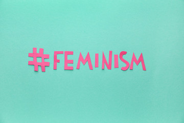 Paper word FEMINISM with hashtag on color background