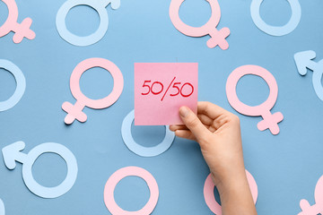 Female hand with paper sheet and symbols of woman and man on color background. Concept of feminism