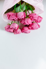 Flower bouquet of pink roses and other mixed flowers wrapped in soft pink paper. Close up, white background. Upside down view, copy space