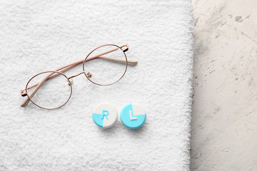 Container with contact lenses and glasses on towel