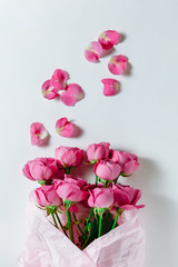 Flower bouquet of pink roses and other mixed flowers wrapped in soft pink paper. The white background is filled with randomly scattered pink petals