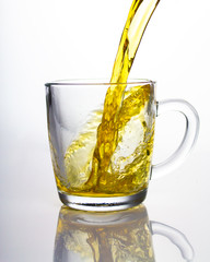A stream of yellow green tea flowing into a transparent glass cup, beautiful spray flying reflection. Pouring tea