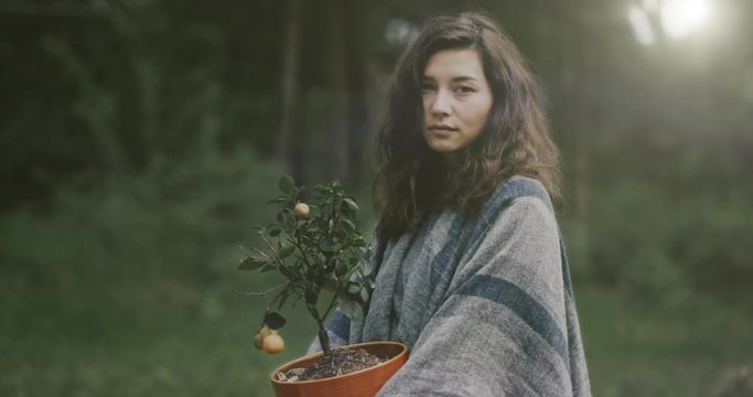 Asian girl holding a pot with a small tree in her hands. Symbol of the green world, vegetarianism, concern for the environment. The video was shot with a 12-bit cinema camera.