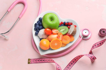 Plate with healthy products, stethoscope and measuring tape on color background