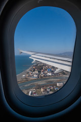 The wing of an airplane flying over the city, the sea and the river . Sochi, Russia