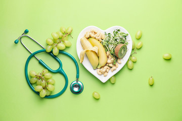 Plate with healthy products and stethoscope on color background