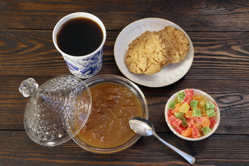 Breakfast. A cup of coffee, cookies, candied fruits and jam on a wooden table.