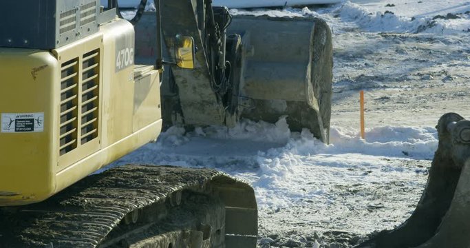Excavtor begins working on construction site in winter - close up on bucket clearing snow