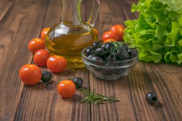 Olives, oil, tomatoes and lettuce on a wooden table.