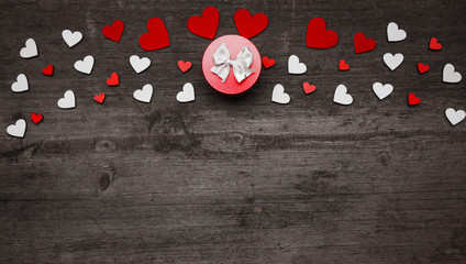 Obraz premium A small round red gift box with a bow on a dark wooden background. Place for text